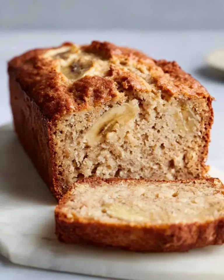 Slice of gluten-free banana bread topped with nuts on a wooden table