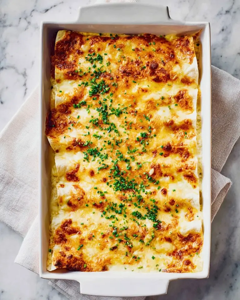 Cheesy chicken enchiladas topped with white sauce and garnished with cilantro